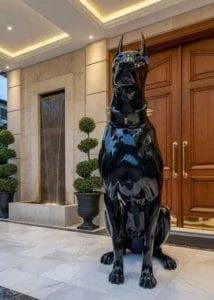 Escultura monumental de un perro Dóberman en acabado negro piano brillante con collar dorado, ubicada en la entrada de una residencia de lujo, fabricada mediante impresión 3D por CR Studio 3D en Medellín.