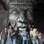 El equipo de trabajo y escultores posando frente a la obra monumental terminada "El Chamán" en la Galería Origen de la Comuna 13, fabricada mediante impresión 3D por CR Studio 3D en Medellín.